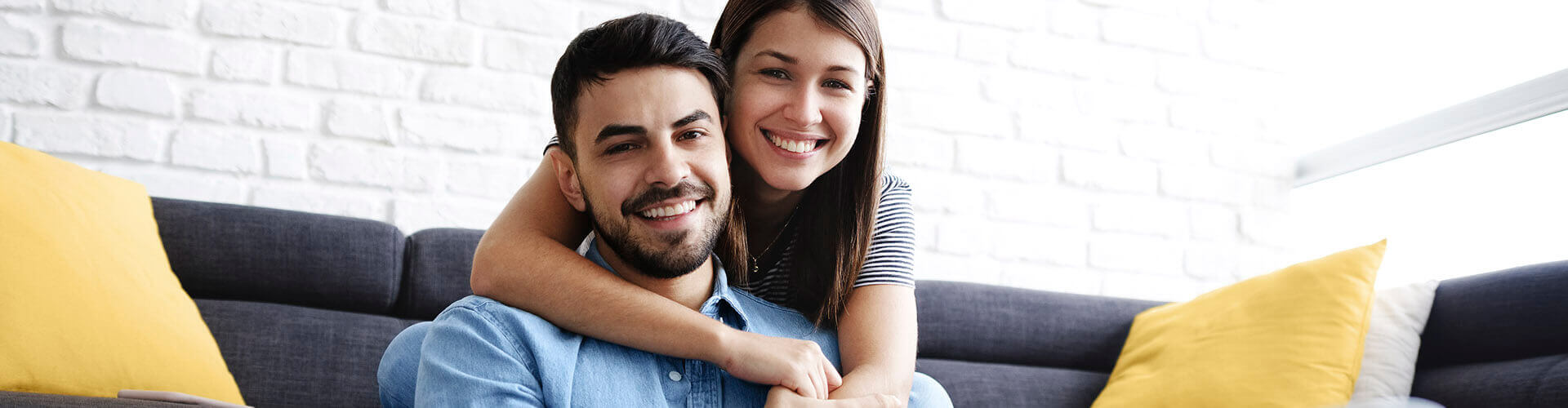 Seguro de Accidentes RGAPersonalPlus - Pareja joven sonriendo en el salón de su casa con portátil Seguro de Accidentes RGAPersonalPlus - Pareja joven sonriendo en el salón de su casa con portátil