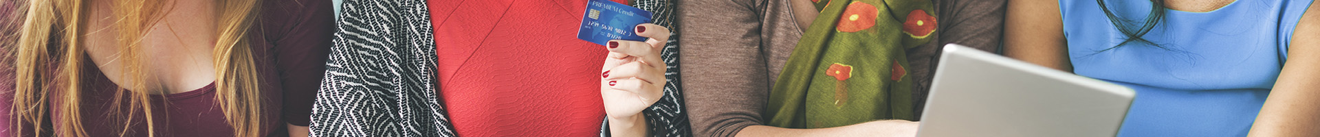Tax Free - Mujeres sentadas en el sofa de casa sonriendo con tarjetas en la mano mirando la tablet Tax Free - Mujeres sentadas en el sofa de casa sonriendo con tarjetas en la mano mirando la tablet