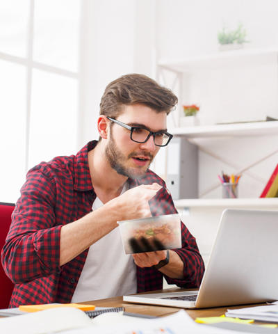 Porque somos así Nómina: Joven comiendo de un Taper ware mientras trabajad en un ordenador portátil