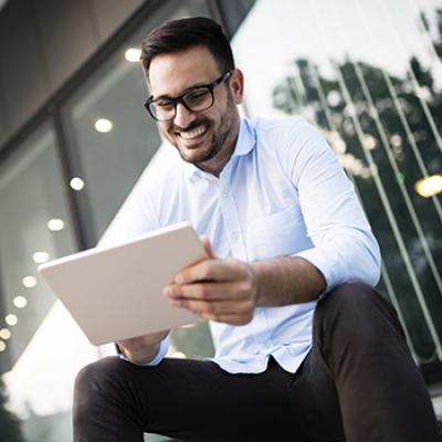 Informe de carteras - Hombre joven con gafas y camisa blanca sentado en la oficina con su tablet viendo informes de mercados