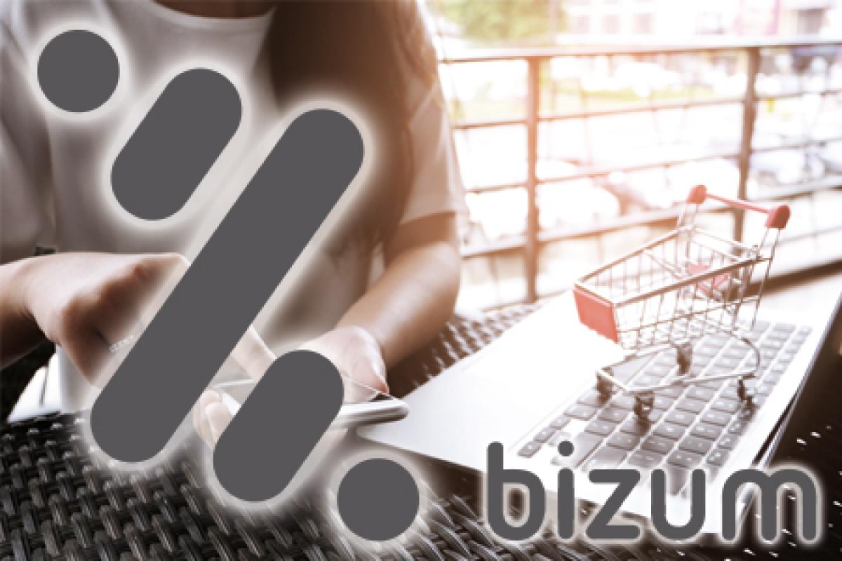 Bizum pago virtual desde el móvil para comercios mujer comprando en un ordenador con el móvil tras el logotipo de bizum